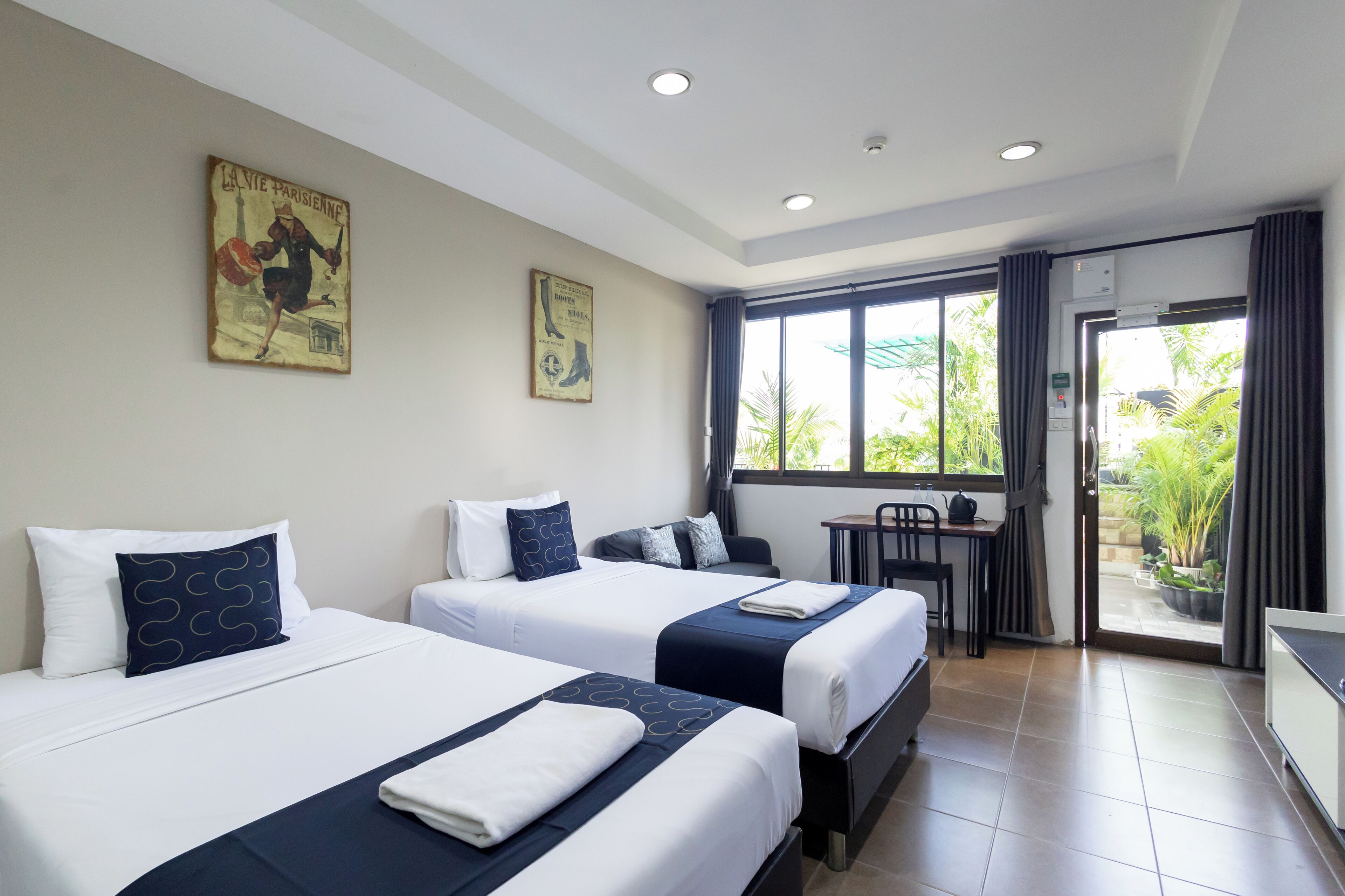 Quarto de hotel com duas camas, uma mesinha e vista para o exterior.