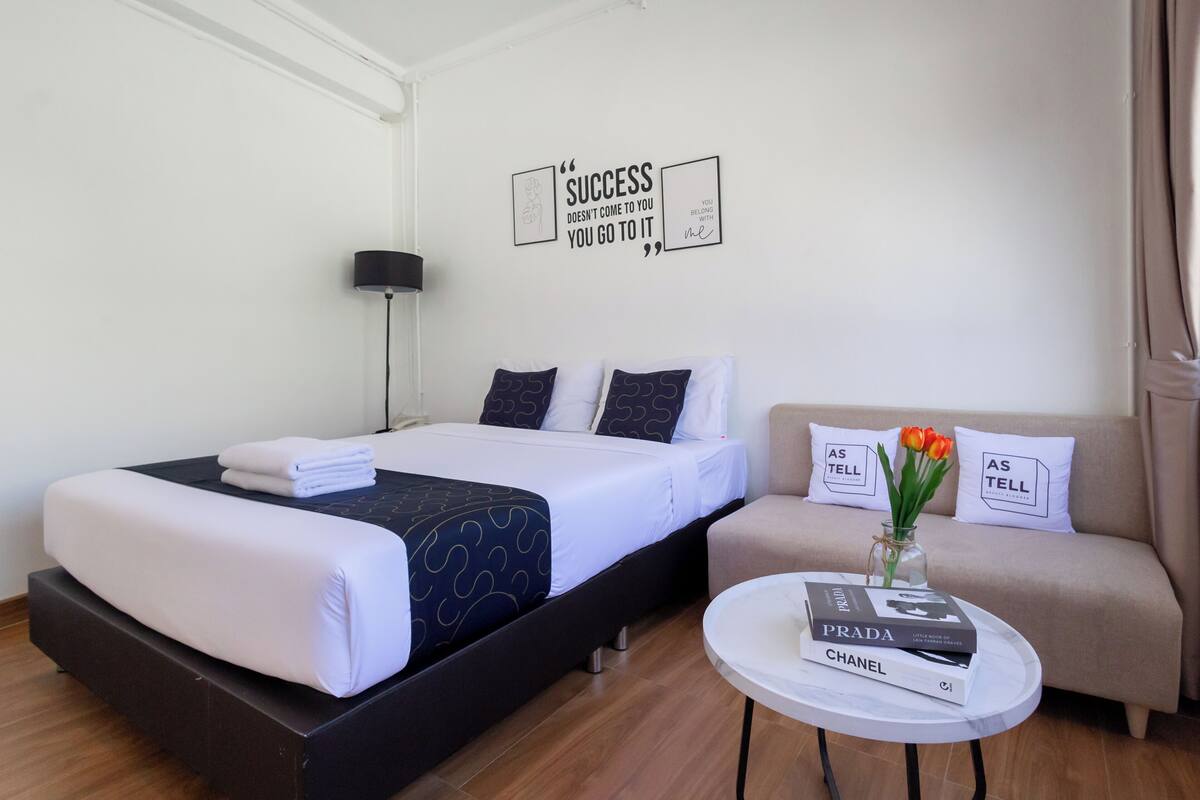 A hotel room with a bed, a sofa, a small table with books, and a motivational quote on the wall.