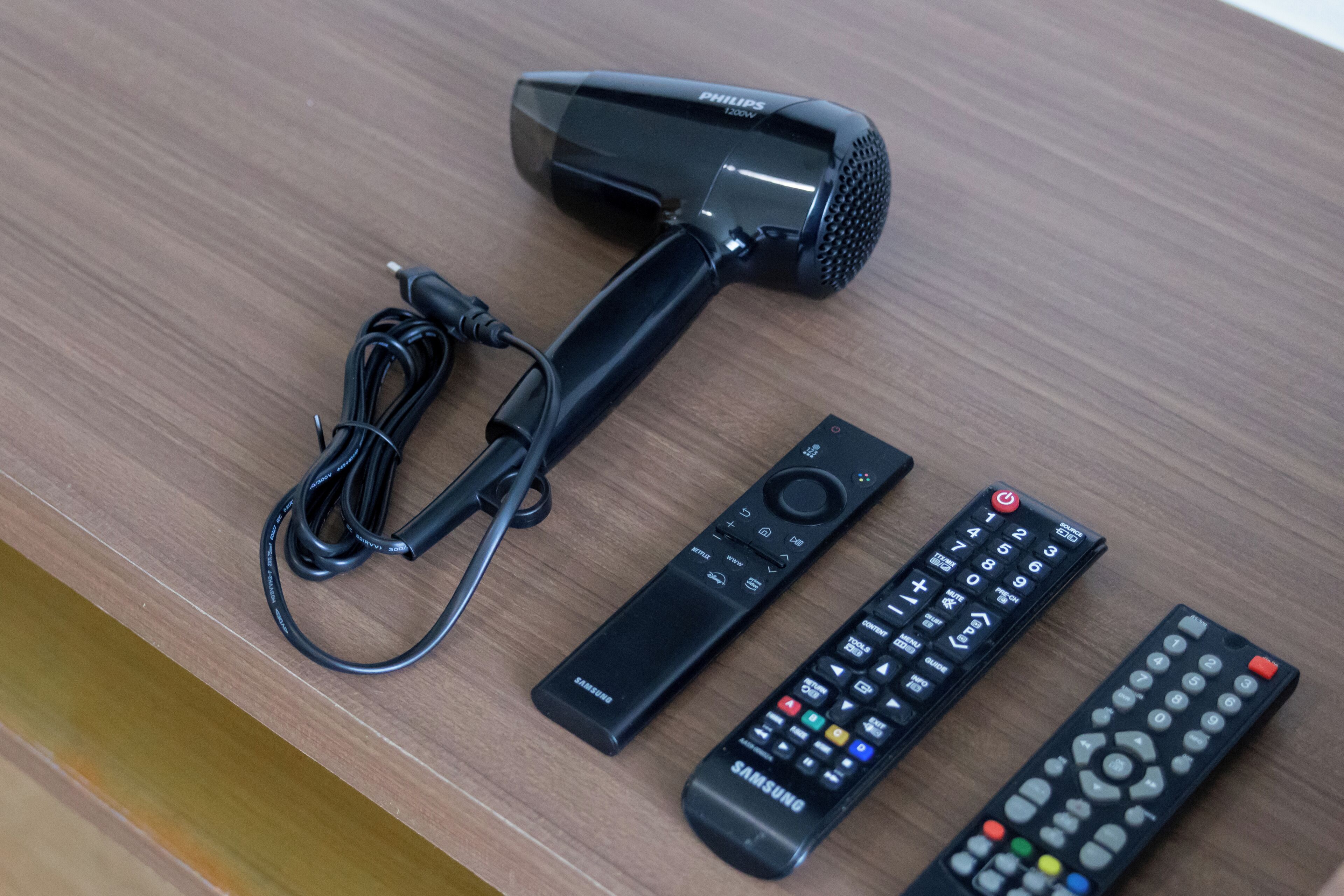 Un sèche-cheveux Philips, une télécommande Samsung et une télécommande universelle, le tout posé sur une surface en bois.
