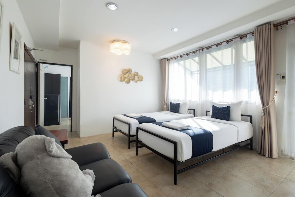 A hotel room with two beds, a sofa, and a large window with curtains.