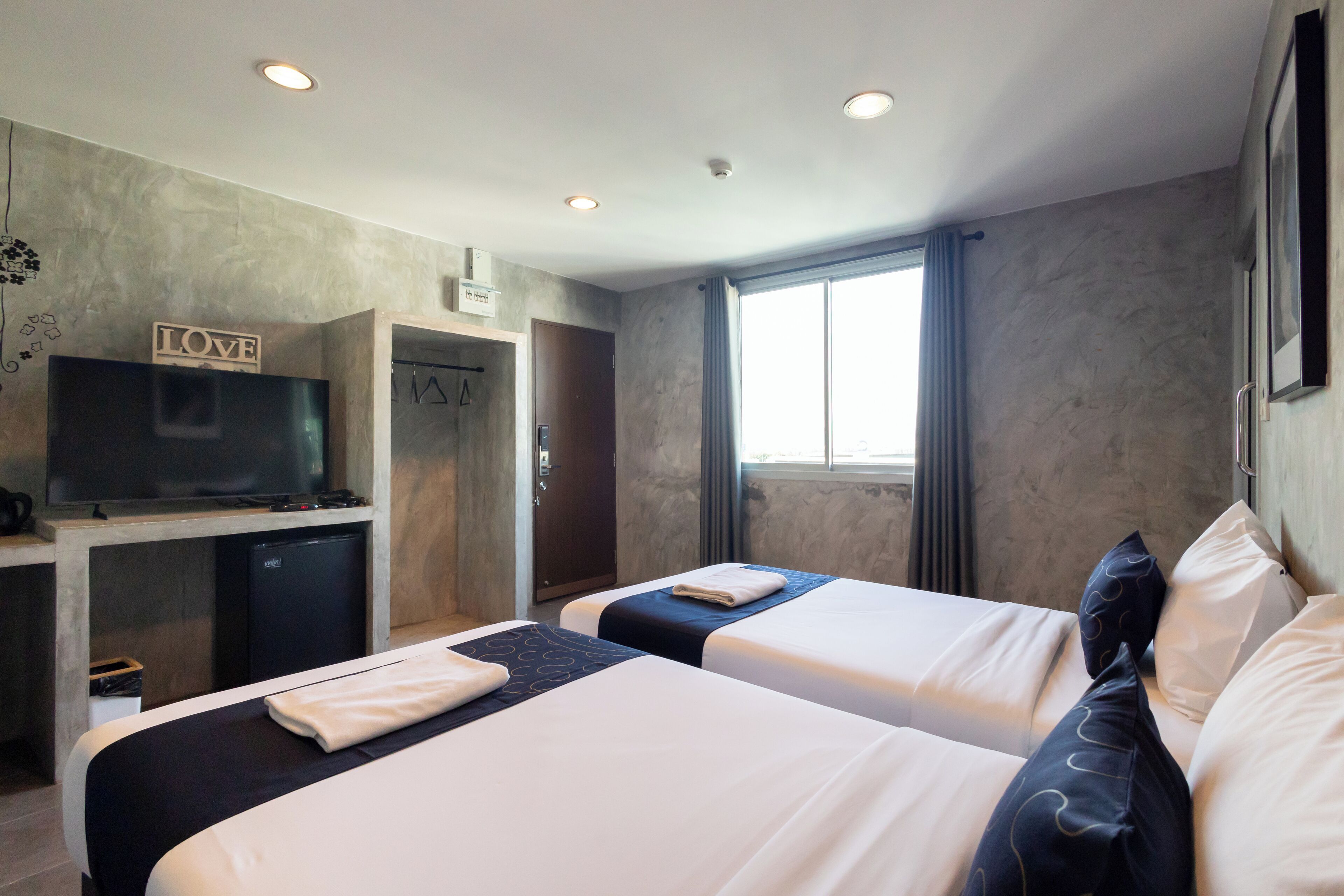 A hotel room with two beds, a TV, a small fridge, and a window with curtains.