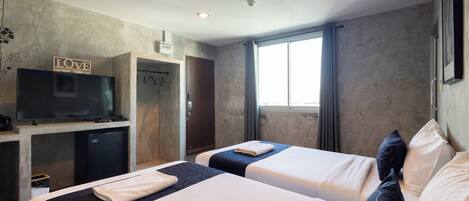 A hotel room with two beds, a TV, a small fridge, and a window with curtains.