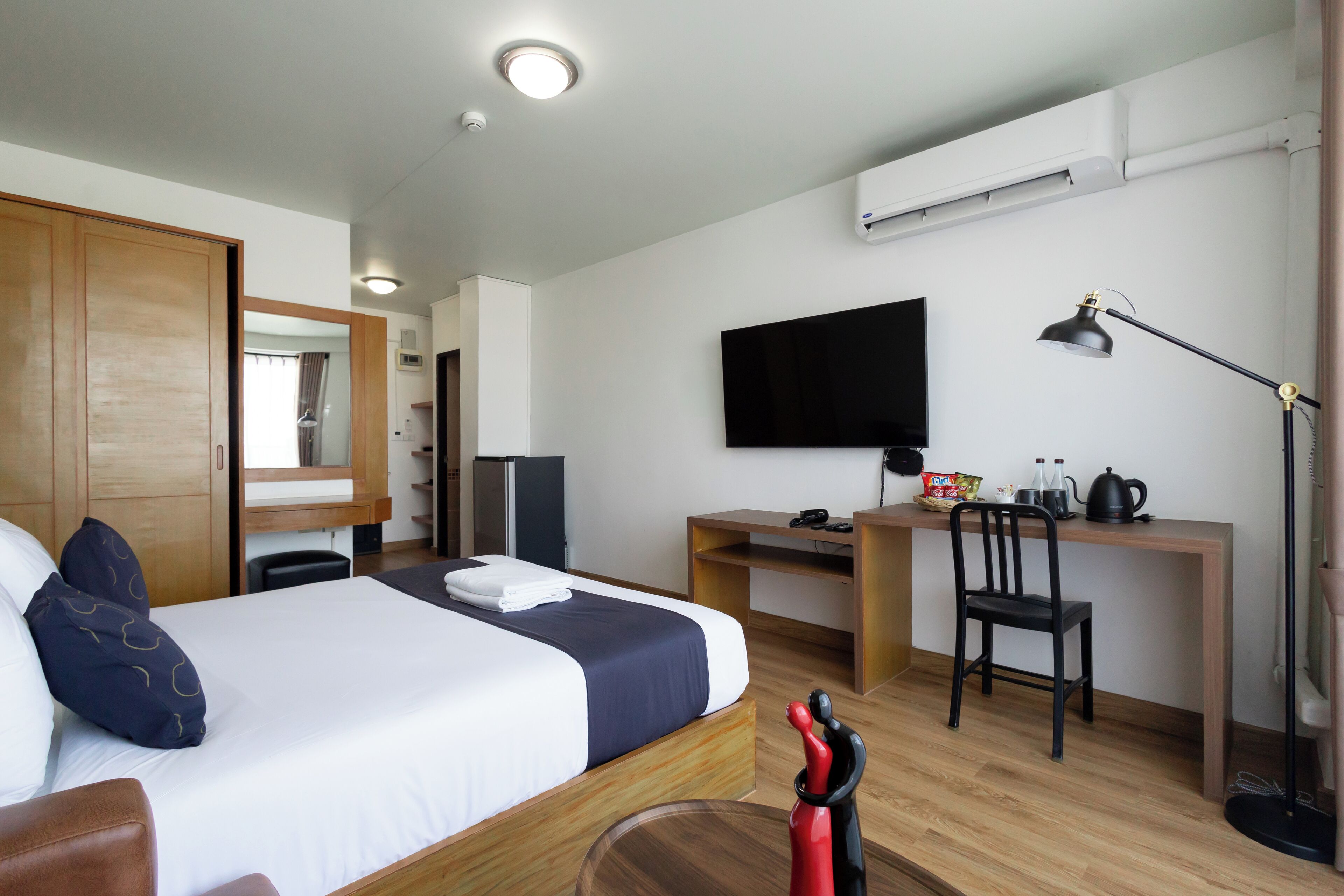 A hotel room with a bed, desk, chair, TV, and a coffee maker.