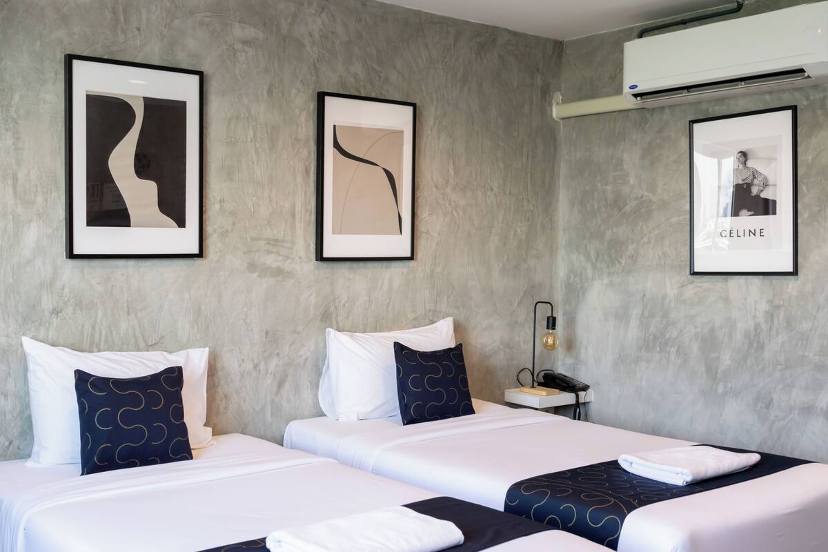 A hotel room with two beds, a nightstand, a lamp, and framed artwork on the walls.