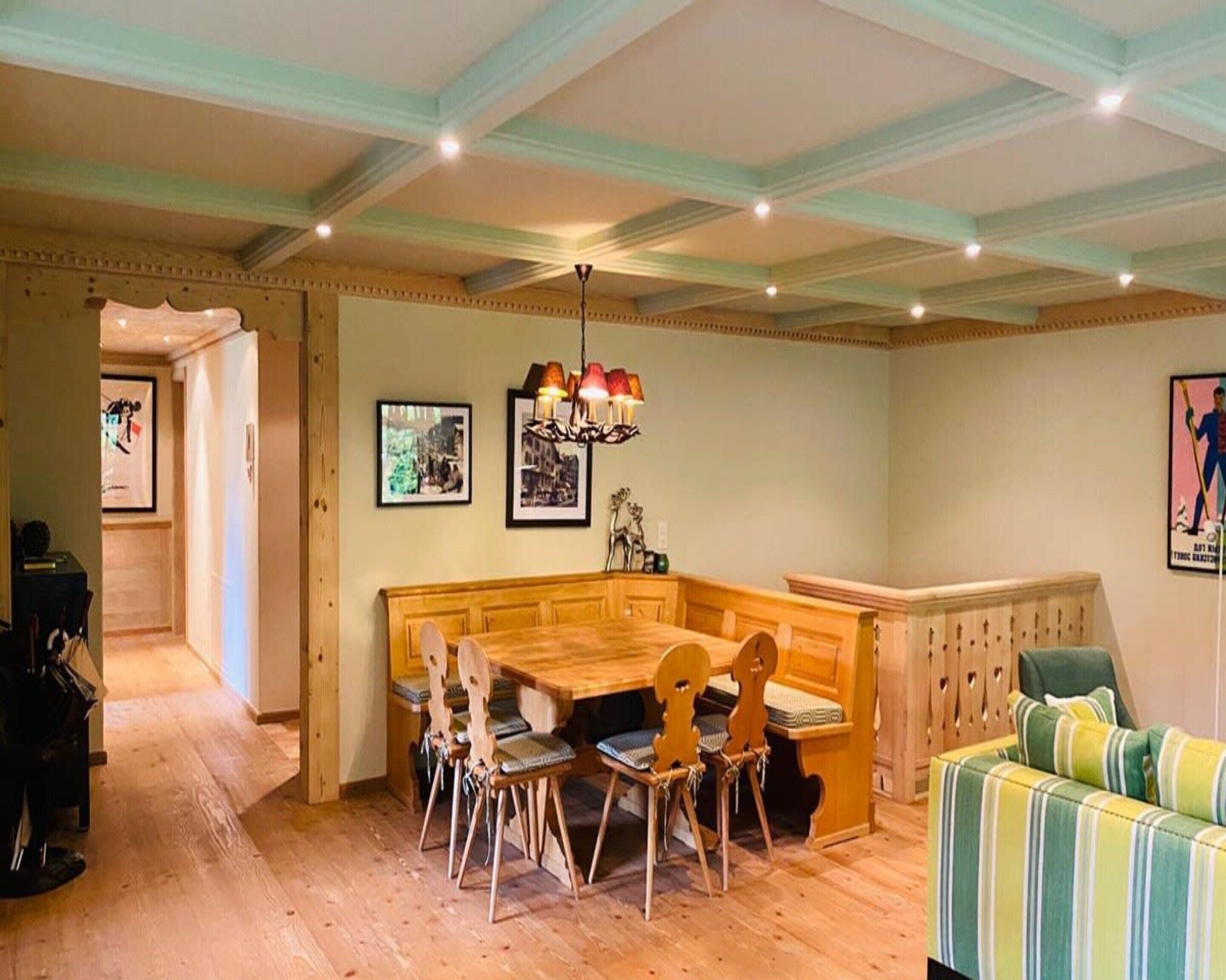 A dining area with a wooden bench and chairs, a chandelier, and framed pictures on the walls.