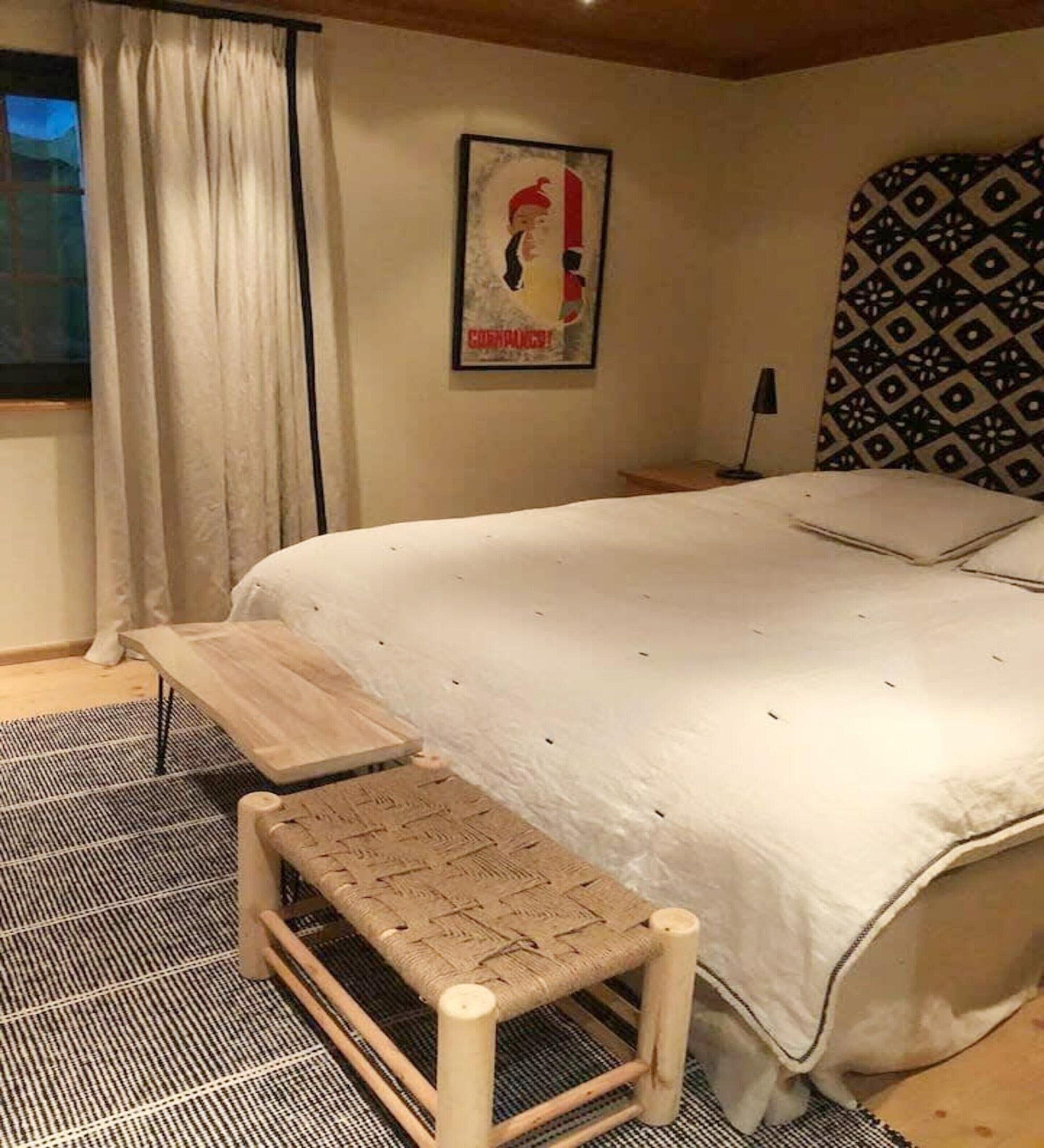 A bedroom with a bed, a small wooden bench, a poster on the wall, and a patterned rug.
