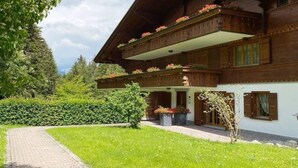 Un chalet traditionnel en bois, doté d’un toit à pente, de balcons ornés de jardinières et d’un chemin pavé menant à l’entrée.
