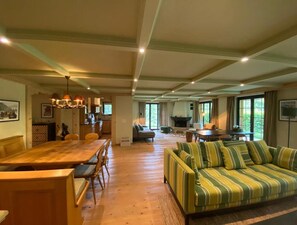 A spacious living area with a wooden dining table, a striped sofa, and a fireplace. - Spa Chalet on Ground Floor (Saanen)