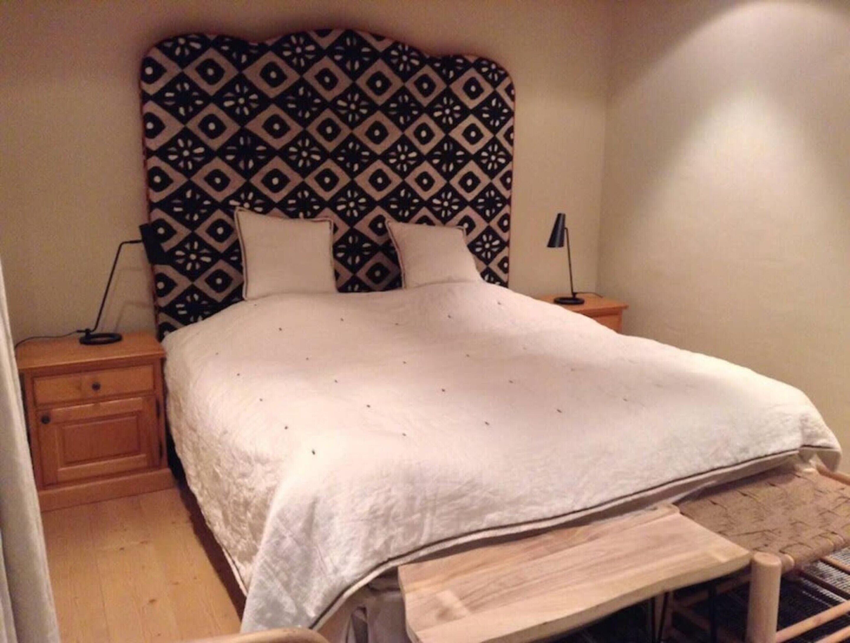 A bed with a patterned headboard, two bedside tables, and a wooden bench.