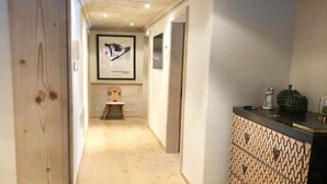 Un couloir étroit au plancher en bois, agrémenté d’une armoire à motifs et de tableaux encadrés accrochés aux murs.
