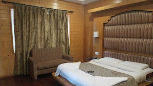 A wooden-paneled room with a bed, a striped armchair, and a window with curtains. - Hotel Mountview Sonamarg (Gund)