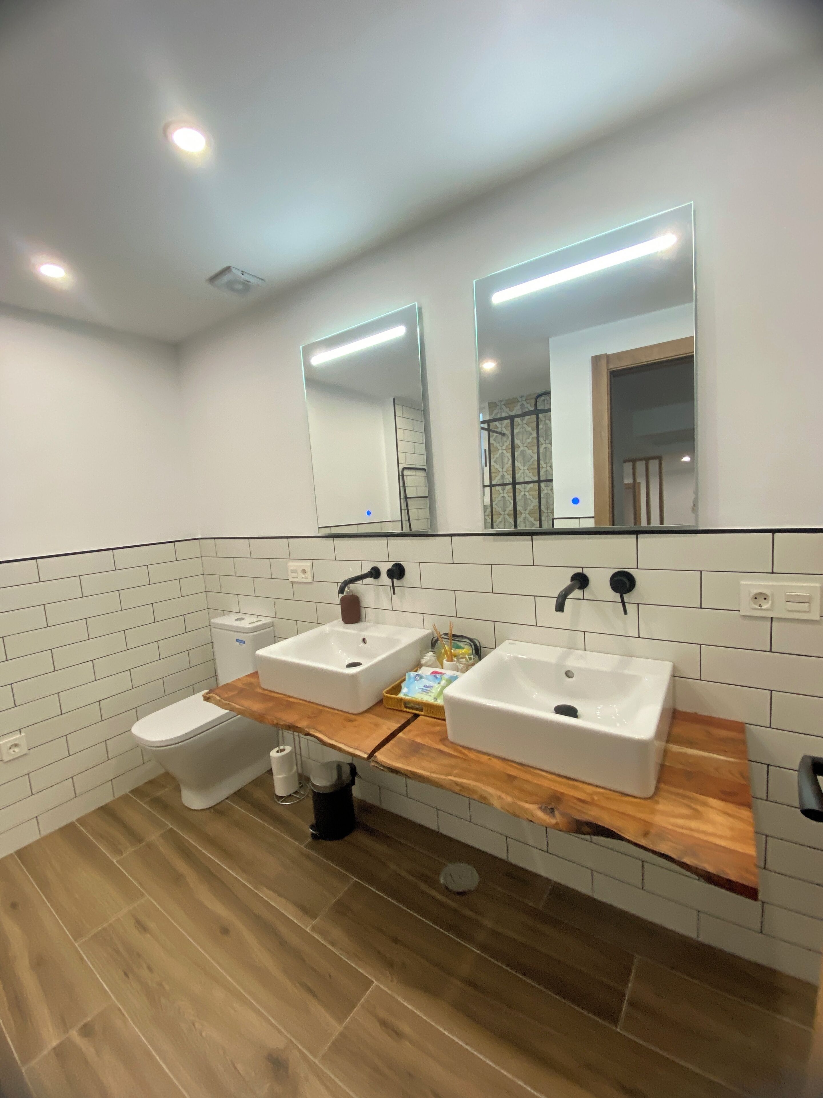 A modern bathroom with two sinks, a toilet, and a mirror.