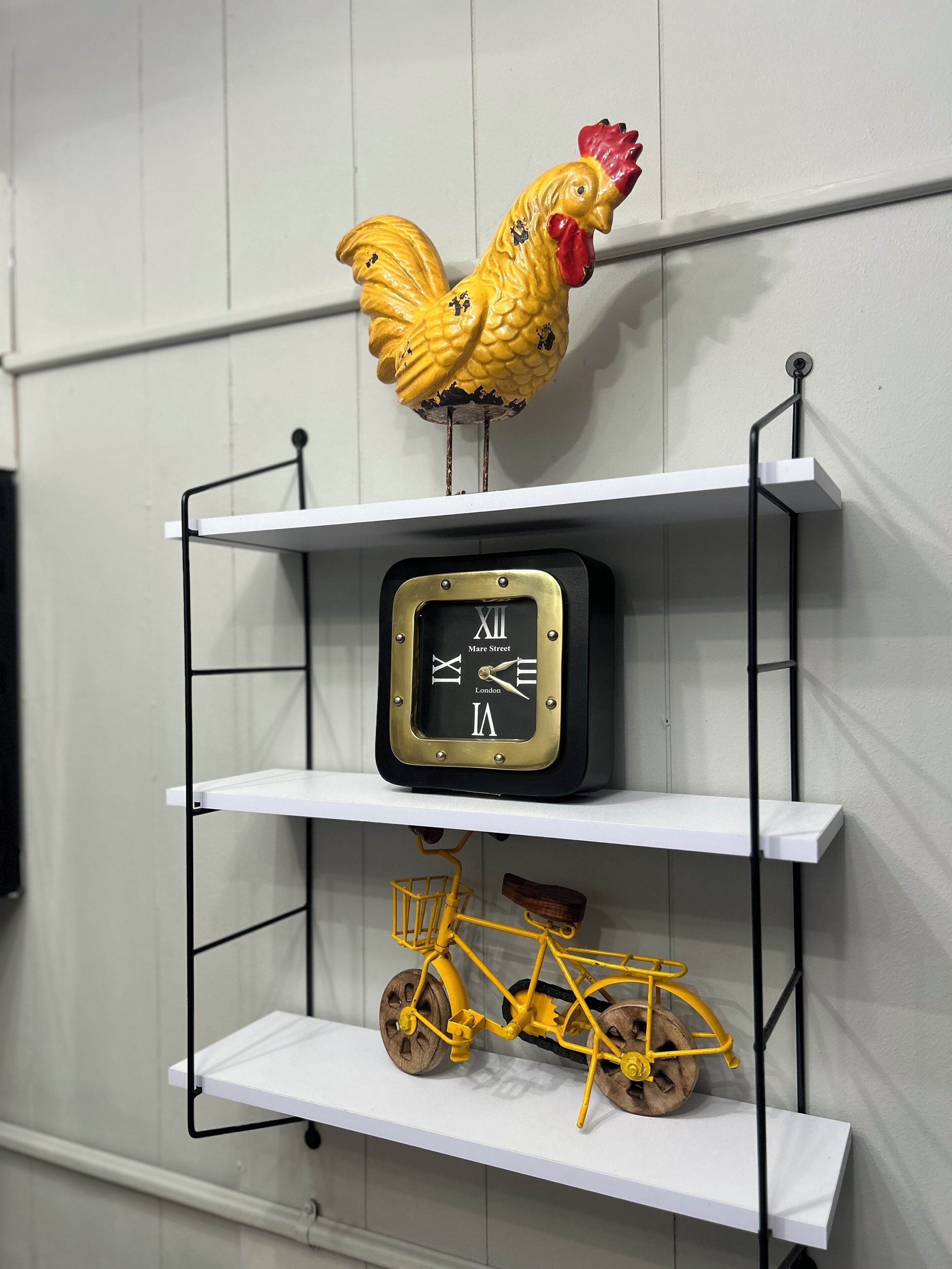 A white metal shelf unit with a decorative rooster, a clock, and a model bicycle.
