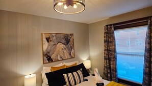 A hotel room with a bed, a painting on the wall, a ceiling light, a bedside table with a lamp, and a window with curtains. - Historic & Chic apartment by Arena, University, Hospital - Dog Friendly (Huntington)