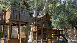 A wooden play structure with multiple levels and platforms, surrounded by trees and greenery. - Bungalow on Spain's Coast With Sandy Beaches (Mont-roig del Camp)