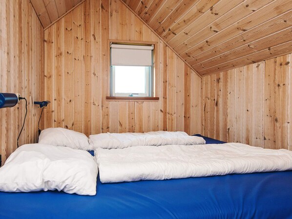 A wooden room with a bed, a window, and a lamp.