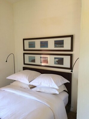 A neatly made bed with white linens and a dark wooden headboard. Above the bed, there are two framed pictures on the wall. - Dar Talmout (Bine el Ouidane)
