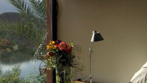 Een nachtkastje met een lamp, een bloemenvaas en uitzicht op water door een raam.