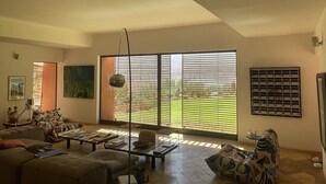 Een ruime woonkamer met een grote schuifpui naar een tuin, een bank, een salontafel en een vloerlamp.