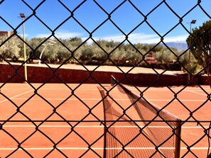 A tennis court with a chain-link fence, surrounded by trees and a clear sky. - Dar Talmout (Bine el Ouidane)