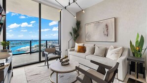 Un salón moderno con sofá, mesa de centro y sillas, un ventanal con vista al mar y un cuadro en la pared.