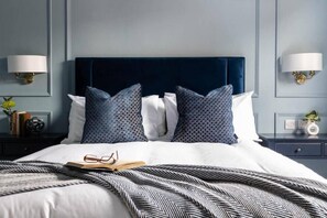 Una cama bien hecha con un edredón estampado, un libro y unos lentes encima.