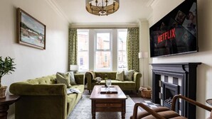 A living room with a green sofa set, a wooden coffee table, a fireplace, and a TV mounted on the wall.