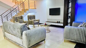 Ein modernes Wohnzimmer mit einer Couch, Sesseln, einem Couchtisch, einem Fernseher und einer Treppe.
