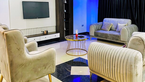 Ein modernes Wohnzimmer mit Flachbildfernseher, einer Couch und zwei Sesseln.