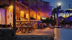 A beachfront resort with a thatched-roof bar area, outdoor seating, and a stone staircase leading to the beach. - Elli Tropical Suites  (Mykonos)