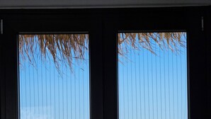 A view through a window with vertical blinds, overlooking a body of water with cruise ships. - Elli Tropical Suites  (Mykonos)