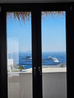 Vista a través de una ventana con persianas verticales, con un cuerpo de agua y cruceros.