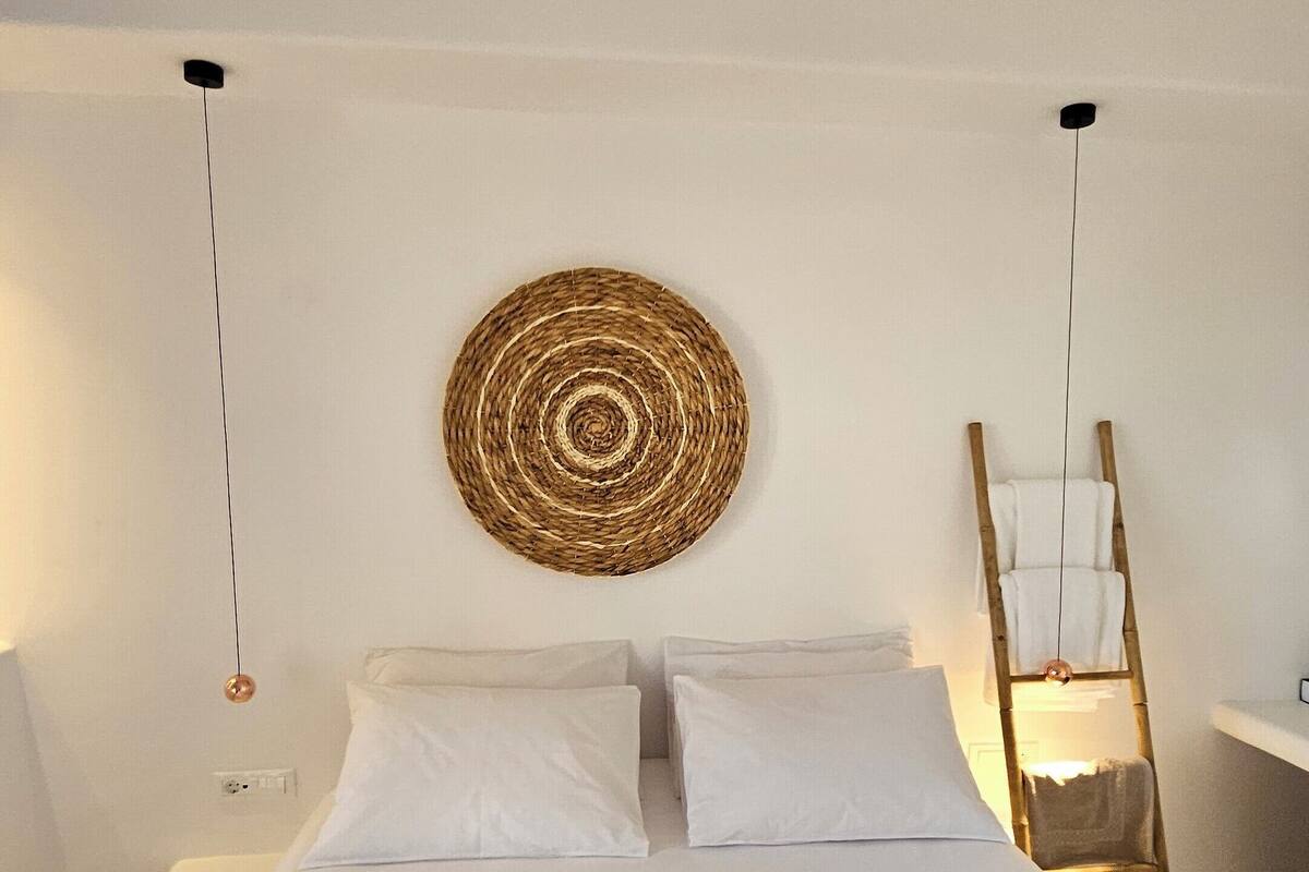 A minimalist bedroom with a large bed, a woven wall hanging, and a ladder with towels.