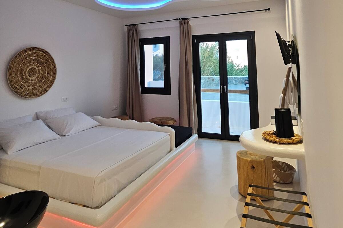 A modern bedroom with a large bed, a small seating area, and a view of the outdoors.
