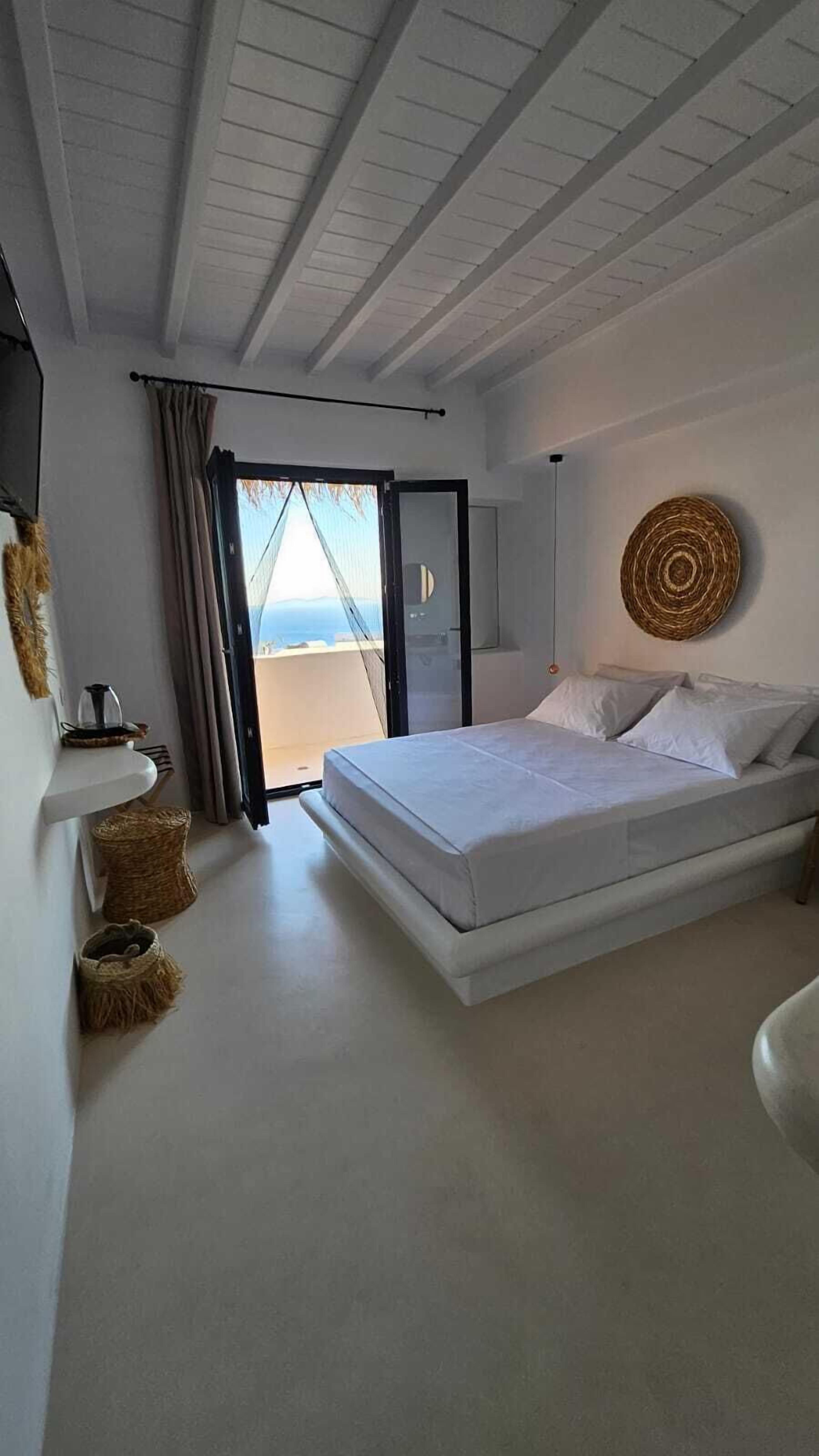 Un dormitorio con una cama, vistas a través de un ventanal y un adorno de pared tejido.