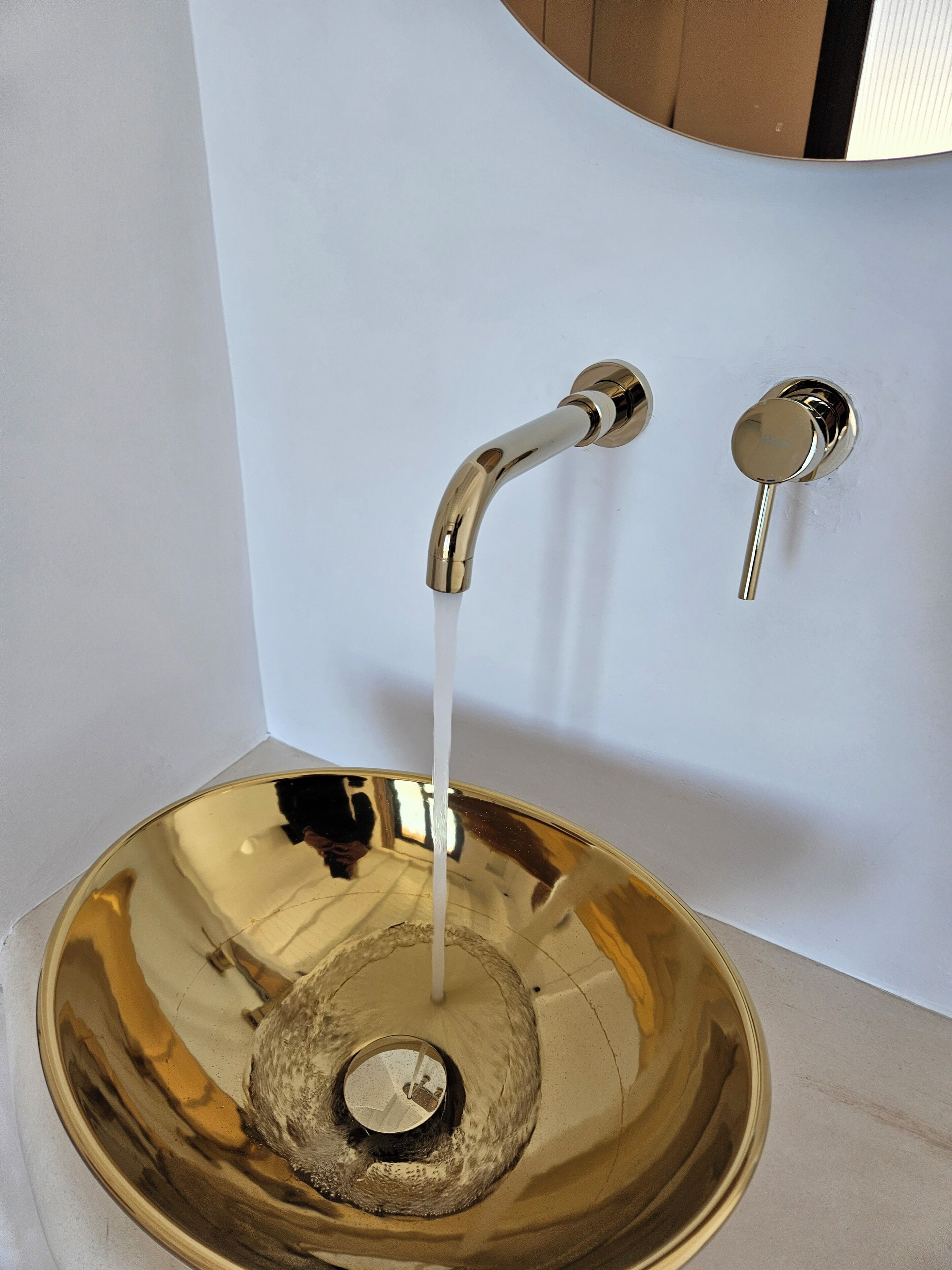 A metallic, bowl-shaped sink with a faucet and a lever handle.