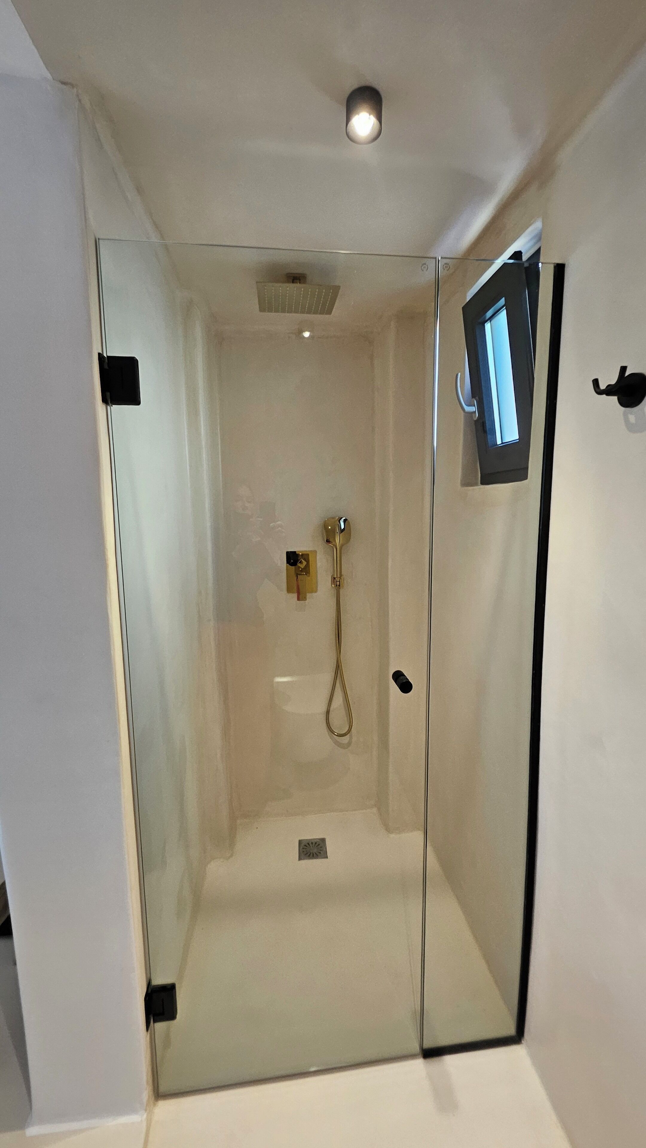 A glass-enclosed shower room with a handheld showerhead, a control panel, and a small window.