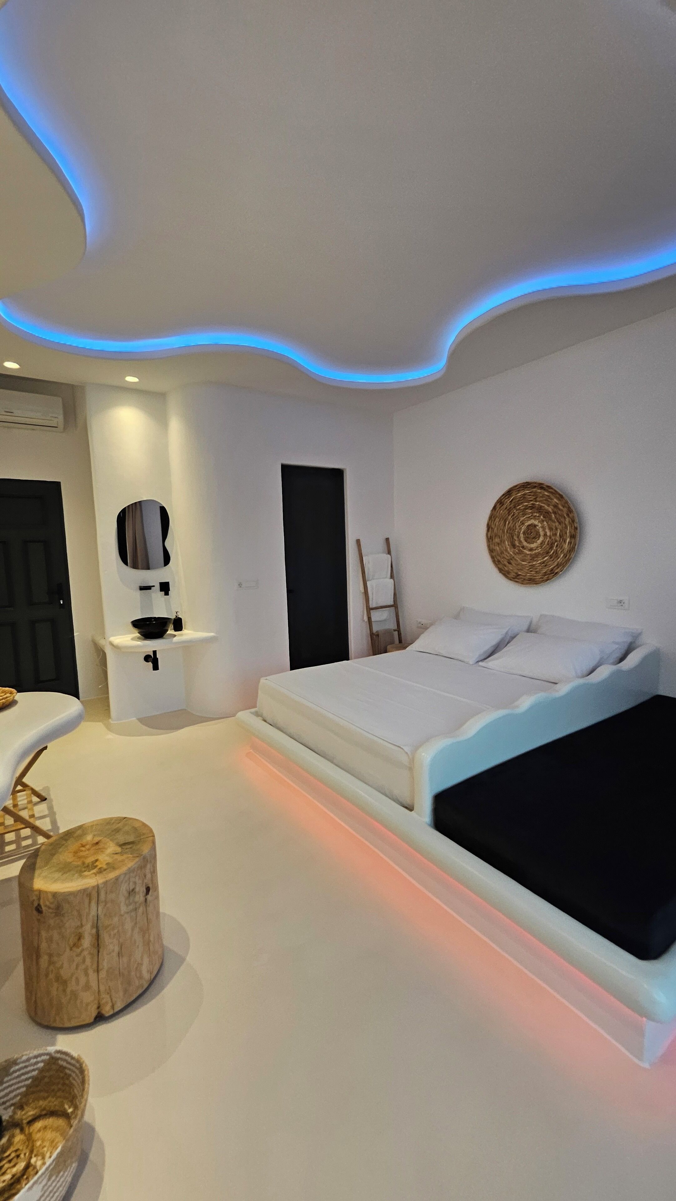 A modern bedroom with a bed, a bedside table, a mirror, a wall-mounted towel rack, and a woven wall art piece.