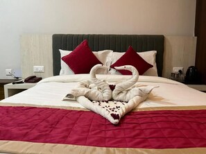Een hotelkamer met een bed, voorzien van een quilt in rood en beige, twee rode kussens, en een decoratieve zwaan van handdoeken.