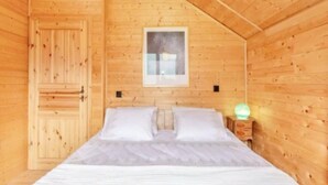 Quarto de cabana de madeira com uma cama, um quadro pendurado na parede e uma mesa de cabeceira com abajur.
