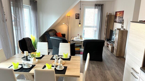 En moderne stue med spiseplads, med en sofa, stole, et sofabord og et fjernsyn.
