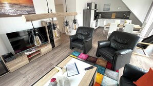 En moderne stue med et fladskærms-tv, sorte læderstole, et farverigt tæppe og et træsofabord.