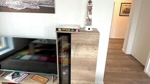 En stue med et fladskærms-tv, et træskab, et billedramme med et solnedgangsmotiv og en lille model af et fyrtårn.