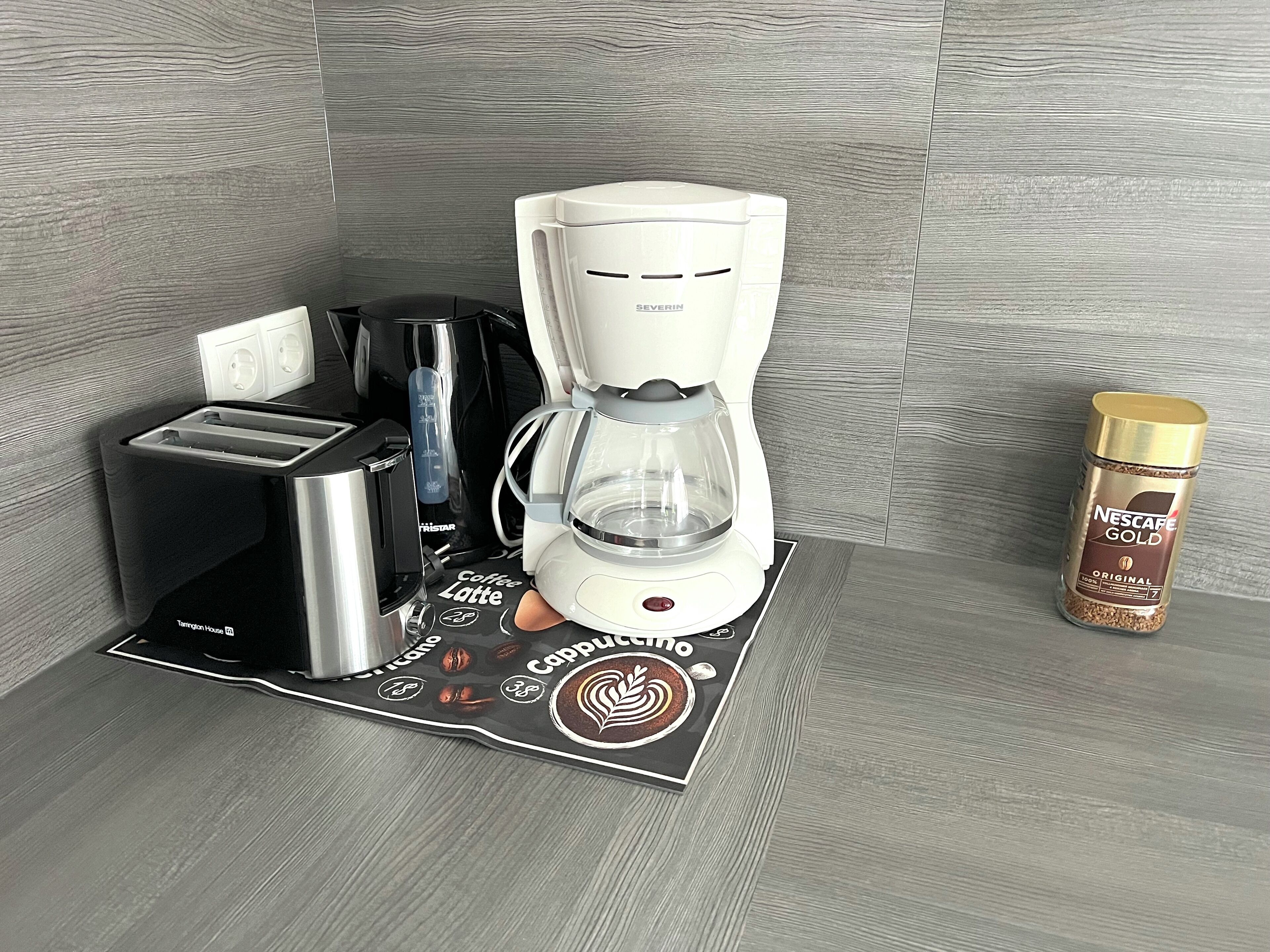 A coffee maker, a coffee grinder, a coffee pod holder, and a Nescafe Gold coffee pod on a countertop.