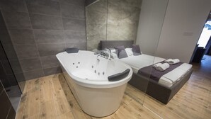 Un baño moderno con una bañera independiente, suelo de madera y una cama con toallas.