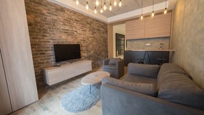 Una sala de estar moderna con una pared de ladrillo, un televisor de pantalla plana, sofás grises, una mesa de centro e iluminación colgante.