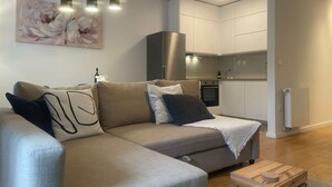 Ein modernes Wohnzimmer mit Sofa, Couchtisch, Pendelleuchten und einer Küchenzeile mit Schränken und Geräten.