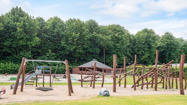 A playground with various play structures, including a slide and climbing frames, surrounded by a grassy area and trees.