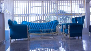A spacious room with a large window, a blue sofa, and matching armchairs. - Hotel Airport View (Lungi)