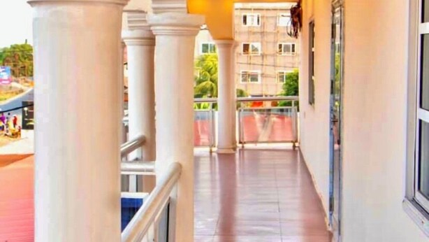 A corridor with white columns, a tiled floor, and a view of a building in the distance. - Hotel Airport View (Lungi)